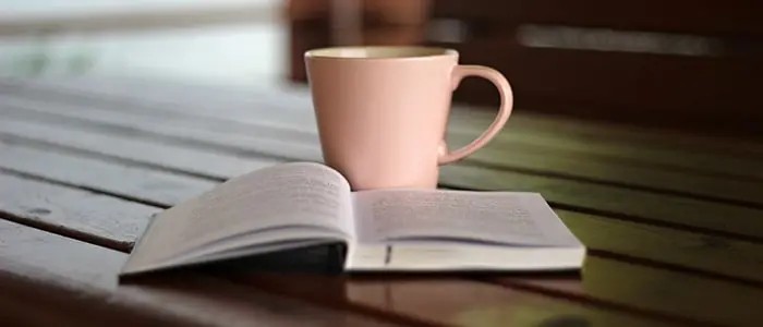 A book placed open on a wooden table, with a cup of tea and glasses nearby, creating a cozy reading atmosphere.