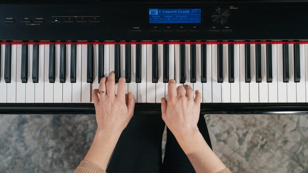 Hands playing chords on a piano keyboard, overhead view focusing on hand position and finger placement.