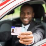 Young man showing his drivers license: Driving age by state and GDL programs