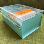 An index card organizing box, with a metal base and a clear plastic lid. Inside are tabbed dividers.