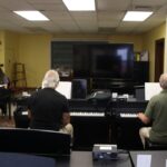 A group piano class in session, showcasing adult learners engaged with keyboards in a classroom setting.