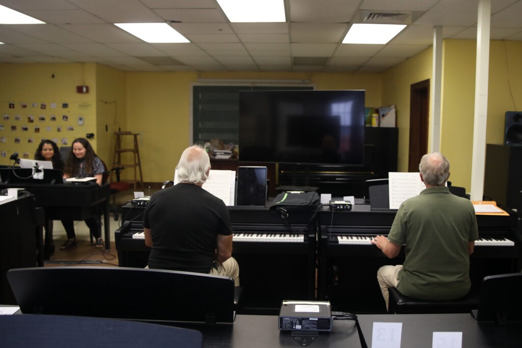 A group piano class in session, showcasing adult learners engaged with keyboards in a classroom setting.