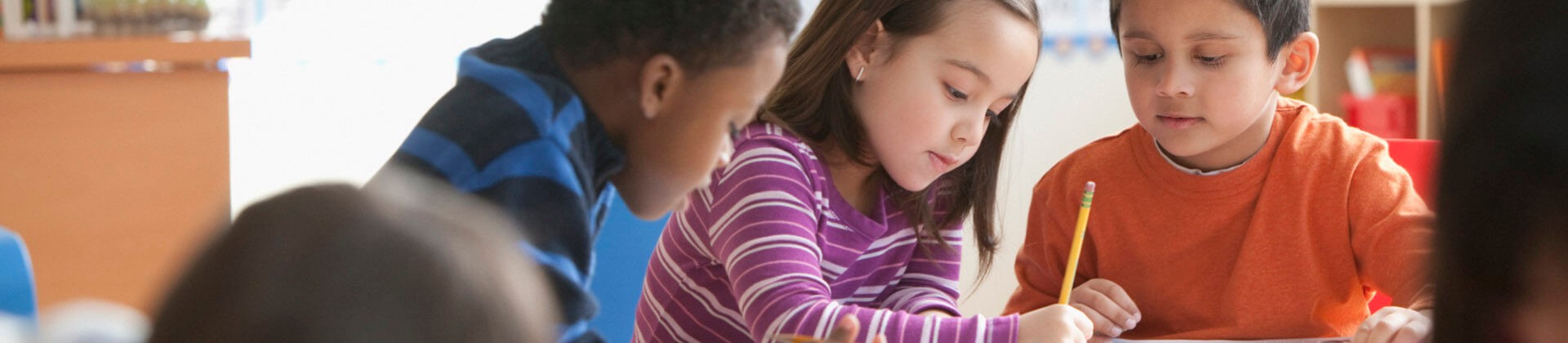 Elementary school children engaged in learning activities, with a girl writing intently while boys observe.