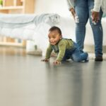 A baby crawling the classic crawl on the floor with mother looking on.