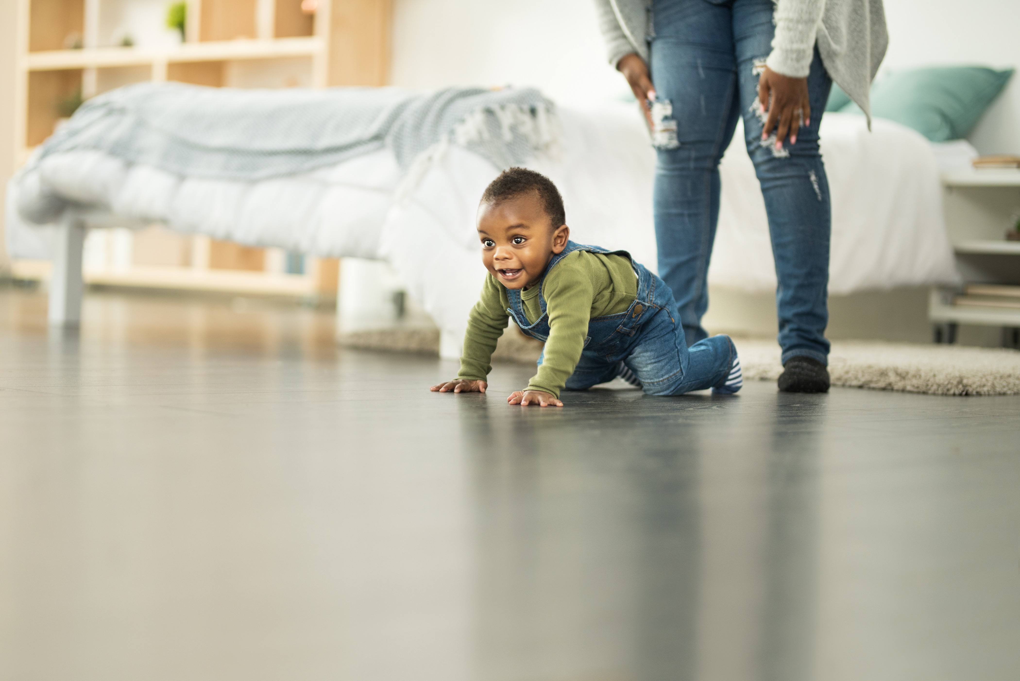 A baby crawling the classic crawl on the floor with mother looking on.