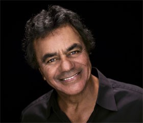 Johnny Mathis performing on stage with the San Francisco Symphony, illustrating his long-lasting career and the valuable lessons of adaptability and continuous excellence.