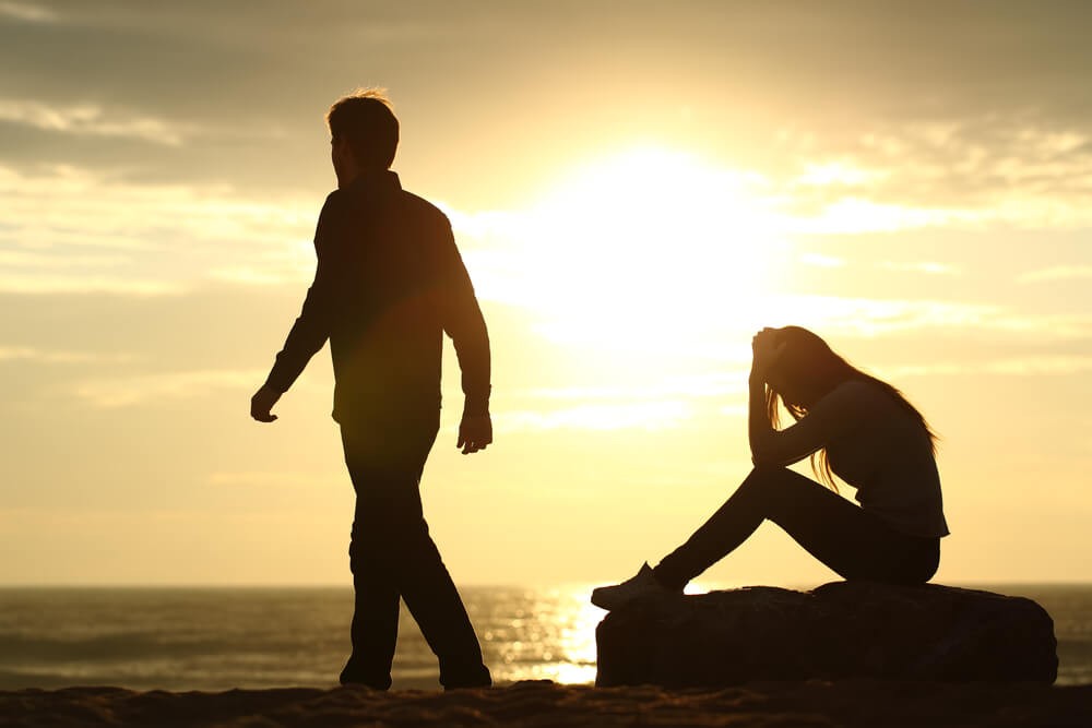 Couple silhouette breaking up a relation on the beach at sunset