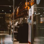 Glass door open to a music store showcasing upright pianos and violins, emphasizing the importance of choosing the right instrument for learning piano.