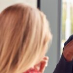 Black professional teacher looking concerningly at student whose back is turned towards camera but appears to be crying