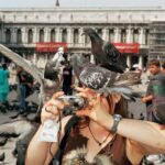 A tourist in Venice, Italy is playfully surrounded by pigeons, showcasing the birds' boldness and adaptability in urban environments, and highlighting interesting animal behaviors to observe and learn from.