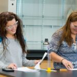 Two female students smiling as they work on a chemistry assignment together.