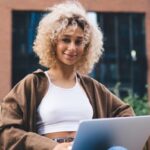 Young woman sitting on a bench with her laptop smiling researching the Spanish language levels