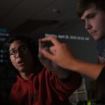 Two male students at PSI High pointing to a reflective screen and practicing higher order thinking skills