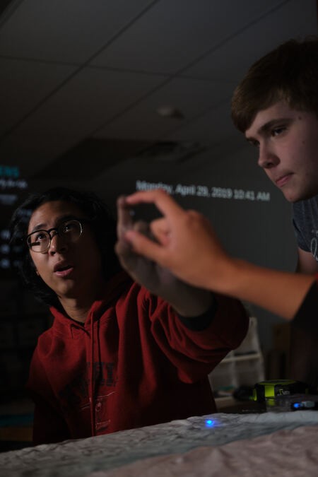 Two male students at PSI High pointing to a reflective screen and practicing higher order thinking skills