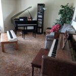 Three pianos in a home setting, showcasing a digital keyboard, an upright piano, and a grand piano.