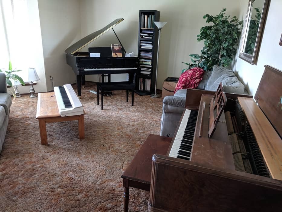 Three pianos in a home setting, showcasing a digital keyboard, an upright piano, and a grand piano.