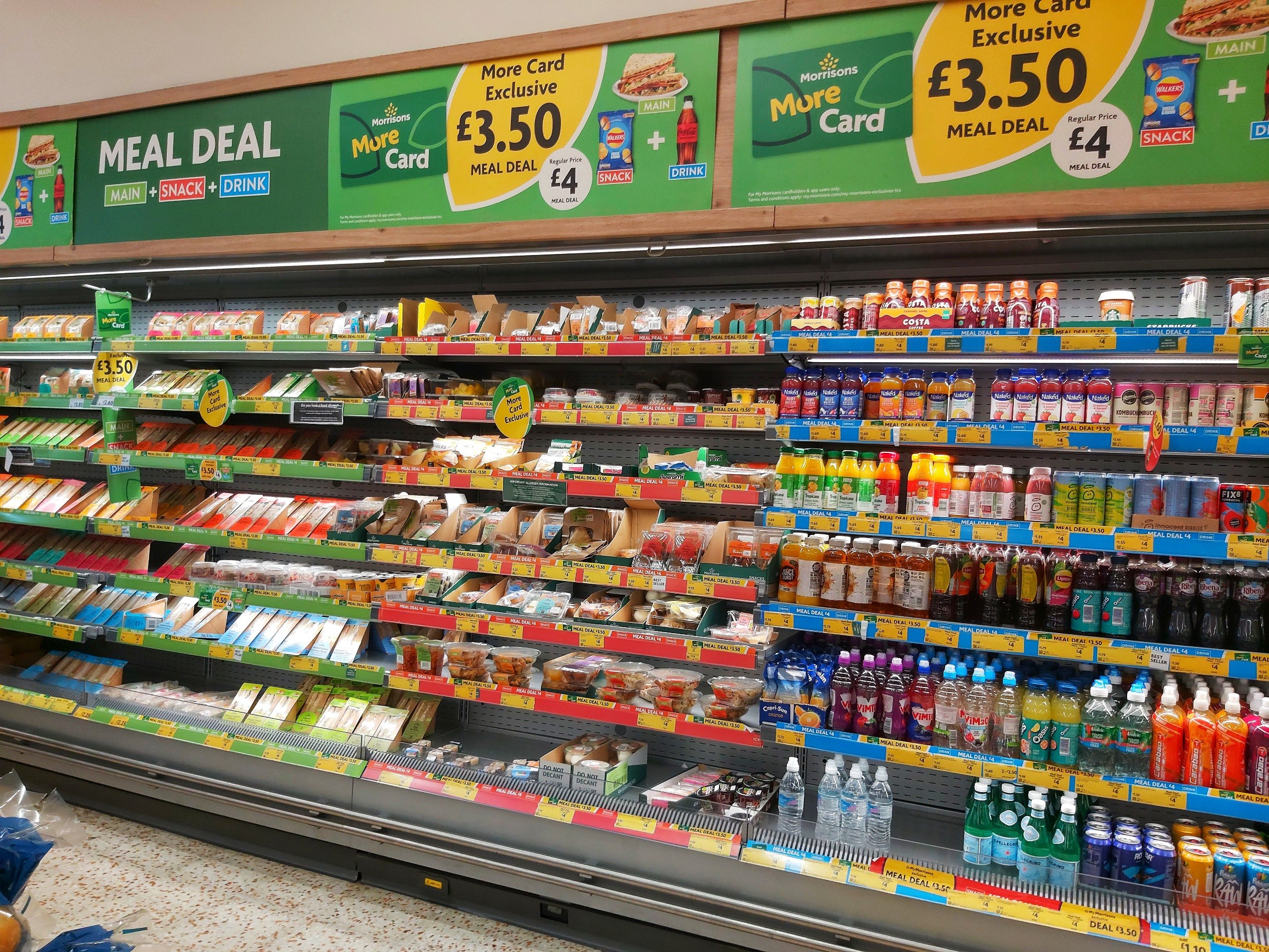 Shelves of meal deal options in Morrisons supermarket, UK. Full fridges filled with soft drinks and packaged sandwiches and salads.