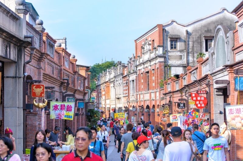 A group of people happily conversing in a bustling Chinese market illustrates the dynamic and engaging experience of communicating with native speakers