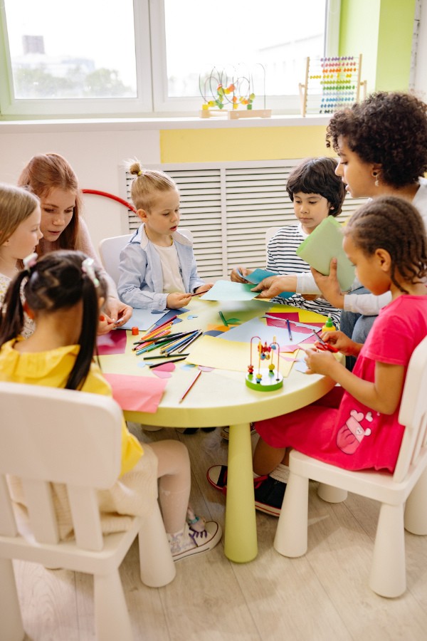 Diverse group of young students happily participating in a classroom activity, with a teacher guiding them.
