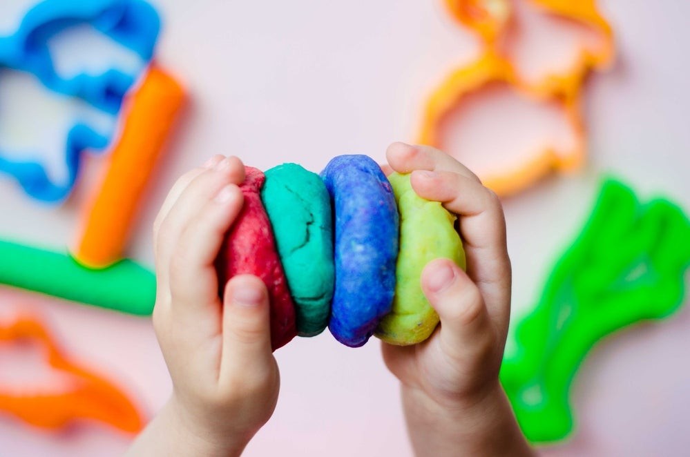 A toddler joyfully squishing colorful play dough, emphasizing sensory exploration and fine motor skills