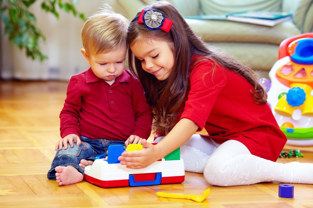 A young girl assisting her 2-year-old brother, highlighting sibling interaction and collaborative play