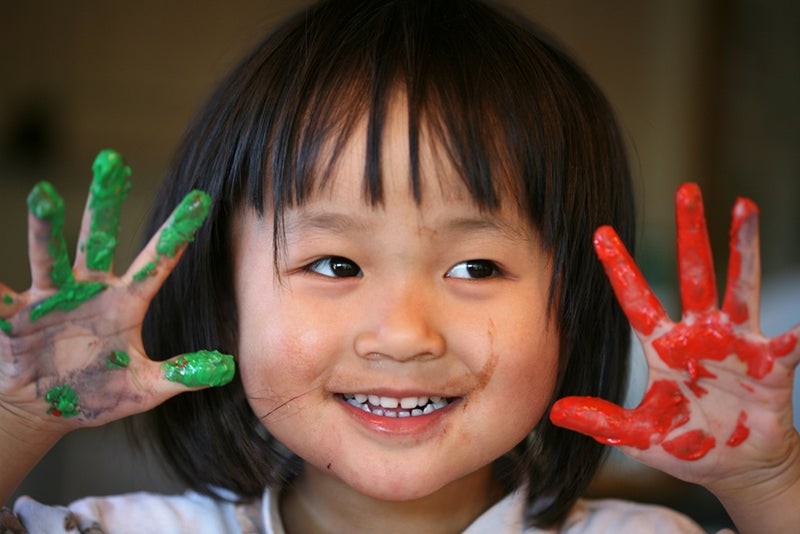 Child deeply focused while creating art with bright finger paints, emphasizing the importance of sensory experiences in early learning