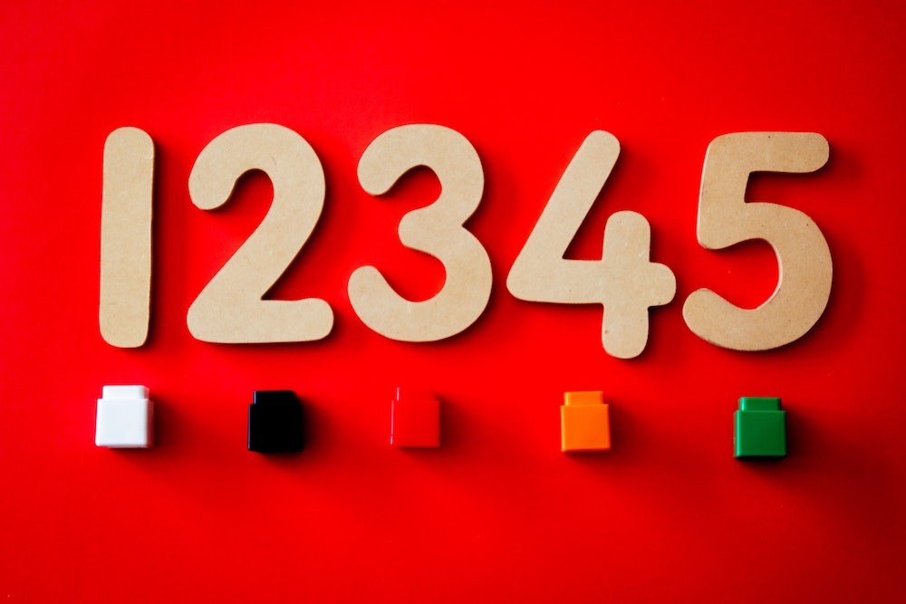 A child is counting blocks while sitting on the floor, with a parent nearby offering guidance and encouragement, to enhance their early math skills and number recognition.