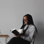 Smiling Person Holding Open Book and Mug