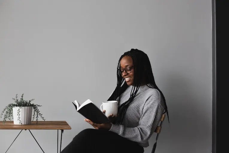 Smiling Person Holding Open Book and Mug