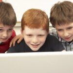 A young boy smiles at a laptop screen while playing an educational game