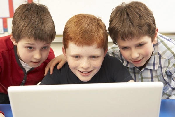 A young boy smiles at a laptop screen while playing an educational game