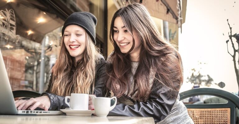 Two female friends looking at a laptop over coffee and practice the hardest words in Spanish
