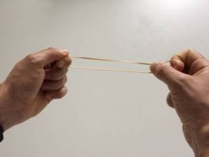 Two hands stretching a rubber band, illustrating how vocal cords work to produce different pitches