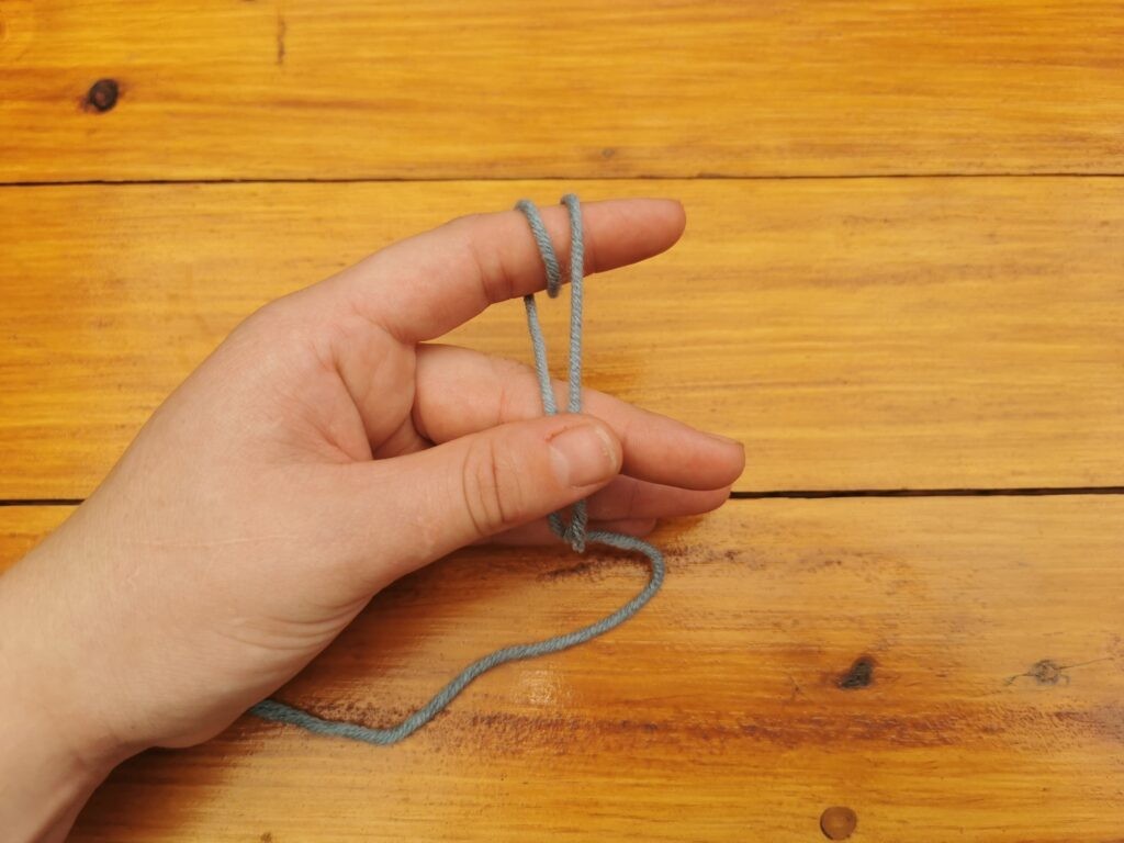 Grab both ends, the short tail attached to the ball of yarn, also known as the working yarn, with your thumb and middle finger.