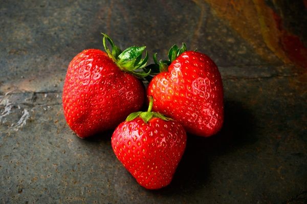 Close-up of a vibrant strawberry, with a blurred background of a fruit stand in Mexico