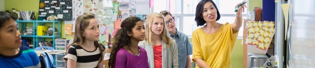 Teacher instructing students on a whiteboard with Social Learning Theory concepts