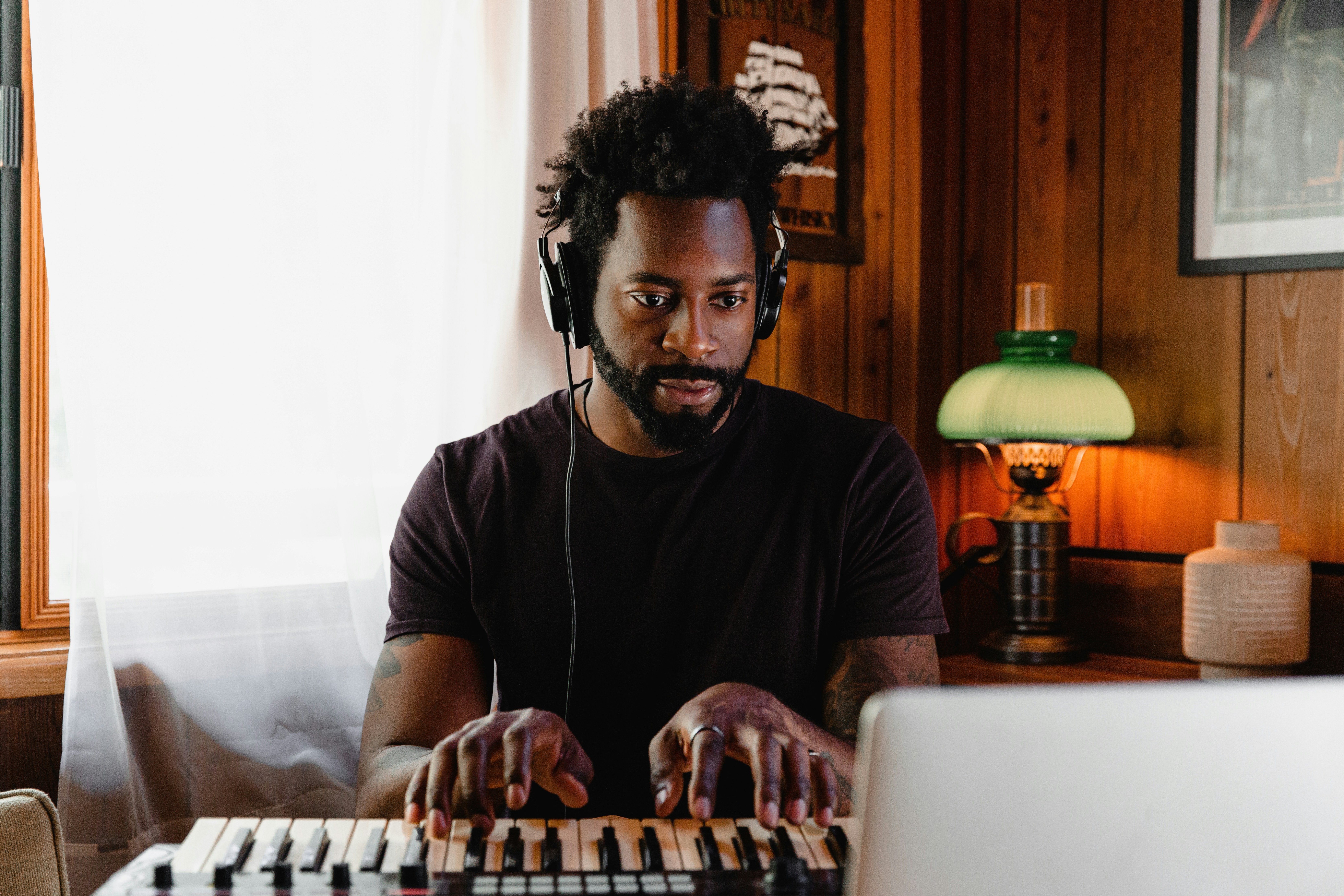 Man with headphones playing piano keyboard on desk in front of a computer screen.