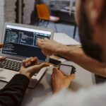 Two people coding on a laptop in an office