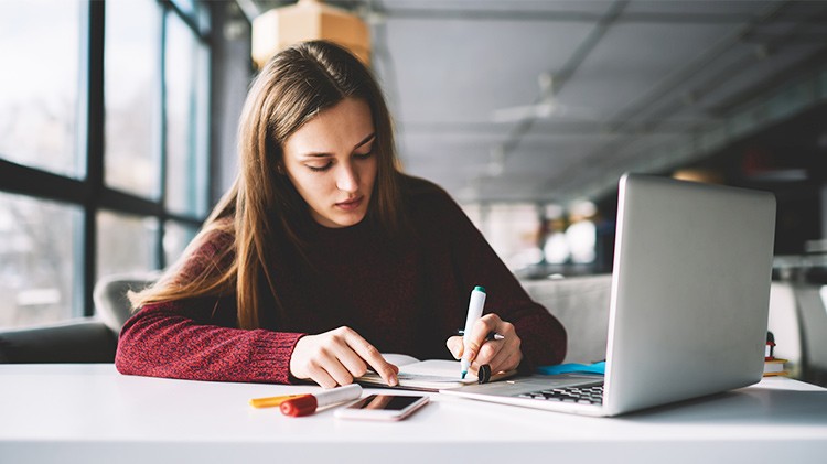 Woman highlighting notes in a library with a laptop